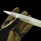 Shining silver double edged narrow blade being held at its' end by a glove covered hand. 

