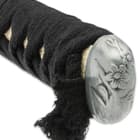 The ornate pommel has a flower design just above the black cord wrapped handle. 