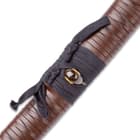 The scabbard has a black hanging cord wrapped around an ornamental piece that matches the brown leather wrapping of the handle.