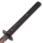 The black faux ray skin handle is wrapped in a black nylon cord with brass menuki peaking out. 