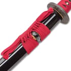 A bright red hanging cord is tied around the glossy black scabbard. 