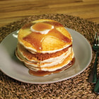 A stack of pancakes from the Emergency Essentials 6-Month Food Kit shown covered in syrup on a green plate with fork.