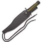The knife is housed in a dark leather sheath, secured by a strap across the guard.