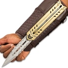 Silver blade with chevron engraving extended over palm of the hand while attached to gold sliding enclosure and mahogany braided faux leather arm sheath.
