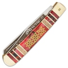 The handle scales are comprised of a burgundy acrylic panel etched with Celtic knotwork, accented with wooden panels