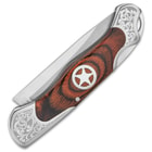 Shown closed, the knife has wooden inserts featuring silver star medallions and polished steel bolsters with etching.
