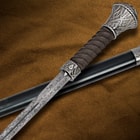 Detailed view of the Damascus steel blade and leather wrapped handle with the cane scabbard in the background. 