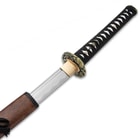 The high carbon steel blade of the katana is shown sliding into its scabbard with view of the black cord wrapped handle.