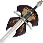Zoomed view of the Sword of Strider hanging from a wood plaque, focusing on the metal cross guard and pommel. 