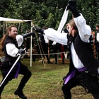 Two men duel at an outdoor festival with rapier swords. 