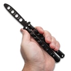 A hand is shown holding the Black Skeleton Butterfly Trainer open with its black skeletonized non-edged blade and handles.