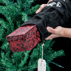 A person is shown holding the black gift bag with ornate box inside next to a Christmas tree. 