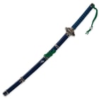The blue scabbard has a green hanging cord, matching the green cord wrapped through the katana’s pommel. 