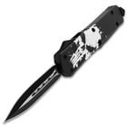 Open OTF pocket knife with dual-toned dagger style blade and a black handle with a large white distressed skull print, glass breaking pommel, and sliding trigger.
