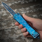A hand grips the handle of the Lightning Blue Auto Knife, with its 4" double-edged stainless steel blade extended and ready for any cutting task.