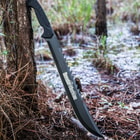The machete is shown in full leaned against a tree, with full view of the “gator tooth” spine blade and textured TPU handle.