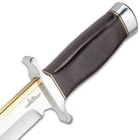 The knife’s hardwood handle is framed by a stainless guard and pommel.
