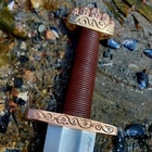 Detailed view of the brass pommel and guard with traditional vine scrollwork, shown on a sandy background.