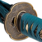 Zoomed view of brass tsuba embossed with double swords on each side showcasing tea dyed rayskin wrapped in a teal cord
