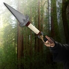 A hand is shown pointing at the Kombat Kunai Thrower on a background of trees.