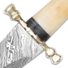 The scalloped brass guard sits just above the unique Damascus steel blade. 