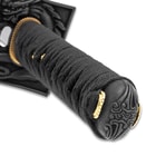 Zoomed view of black nylon wrapped hilt and etched pommel with accents of gold
