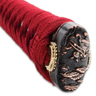 The hardwood handle is traditionally wrapped in faux rayskin and red cord and has an intricately detailed metal tsuba