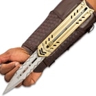 Silver blade with chevron engraving extended over palm of the hand while attached to gold sliding enclosure and mahogany braided faux leather arm sheath.
