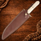 Knife in brown leather sheath on wooden surface with rope
