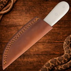 Knife in brown leather sheath on wooden surface