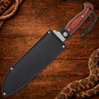 Knife in black sheath on wooden background