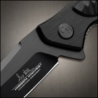 Closed 4 5/8" black pocket knife with scalloped details and a pocket clip with an inscription reading "Hibben Knives."
