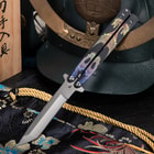 Butterfly knife with dragon design, displayed on decorative fabric