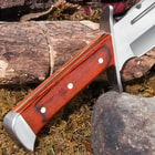 Upclose view of a polished pakkawood handle with silver accents on a background of wood, moss, and rock. 
