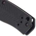 Upclose view of the lanyard opening on the end of the matte black G10 handle with a milled chevron pattern.

