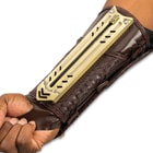 Retracted tactical gauntlet compossed of mahogany brown faux leather and gold blade enclosure attached to the inner forearm.
