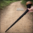 Hand holding a black walking cane with a wooden handle on a dirt path