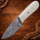 Knife with white handle and patterned blade on wood surface