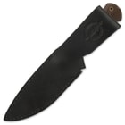 Bushcraft knife enclosed in a black leather belt sheath with a handle strap and "Hibben Knives" stamp. 
