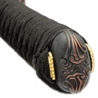 The hardwood handle is wrapped in faux rayskin and black cord and has an intricately detailed metal alloy tsuba