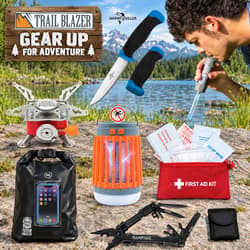 Camping gear including tools, knives, stove, lantern, first aid kit, and dry bag by a lake