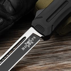 Closed OTF knife with a matte black handle and a pocket clip with a white "M48" logo inscription and a glass breaking pommel.