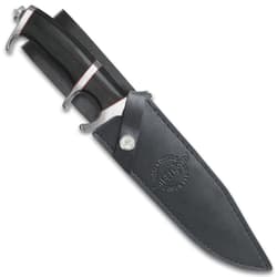 Large knife with black, red, and silver, hilt exposed with the blade enclosed in a black leather sheath stamped with "Hibben Knives" logo