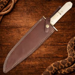 Knife in brown leather sheath on wooden surface with rope