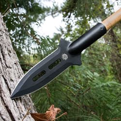 The black spearhead, made of high carbon steel, is shown piercing a tree.