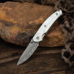 Knife with white handle and Damascus blade on rocky surface