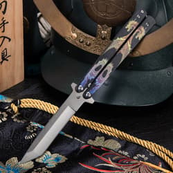 Butterfly knife with dragon design, displayed on decorative fabric