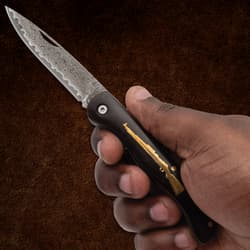 Hand holding a folding knife with patterned blade