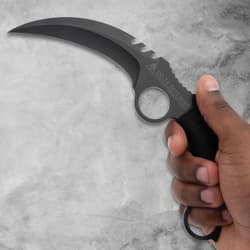 Hand holding a black karambit knife with a curved blade
