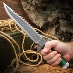 The Rambo I Signature Edition Knife being held in hand. The knife features a polished clip-point blade with a sawback spine